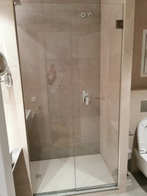 Mampara de ducha batiente a medida en baño revestido de piedra en Barcelona